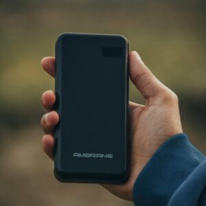 Close-up of a hand holding a portable black power bank outside, showcasing modern technology.