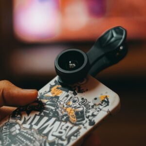 Smartphone with clip-on lens held in hand, capturing close-up shots indoors.