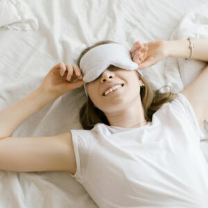A serene young woman enjoying relaxation with a sleep mask in her cozy bed.